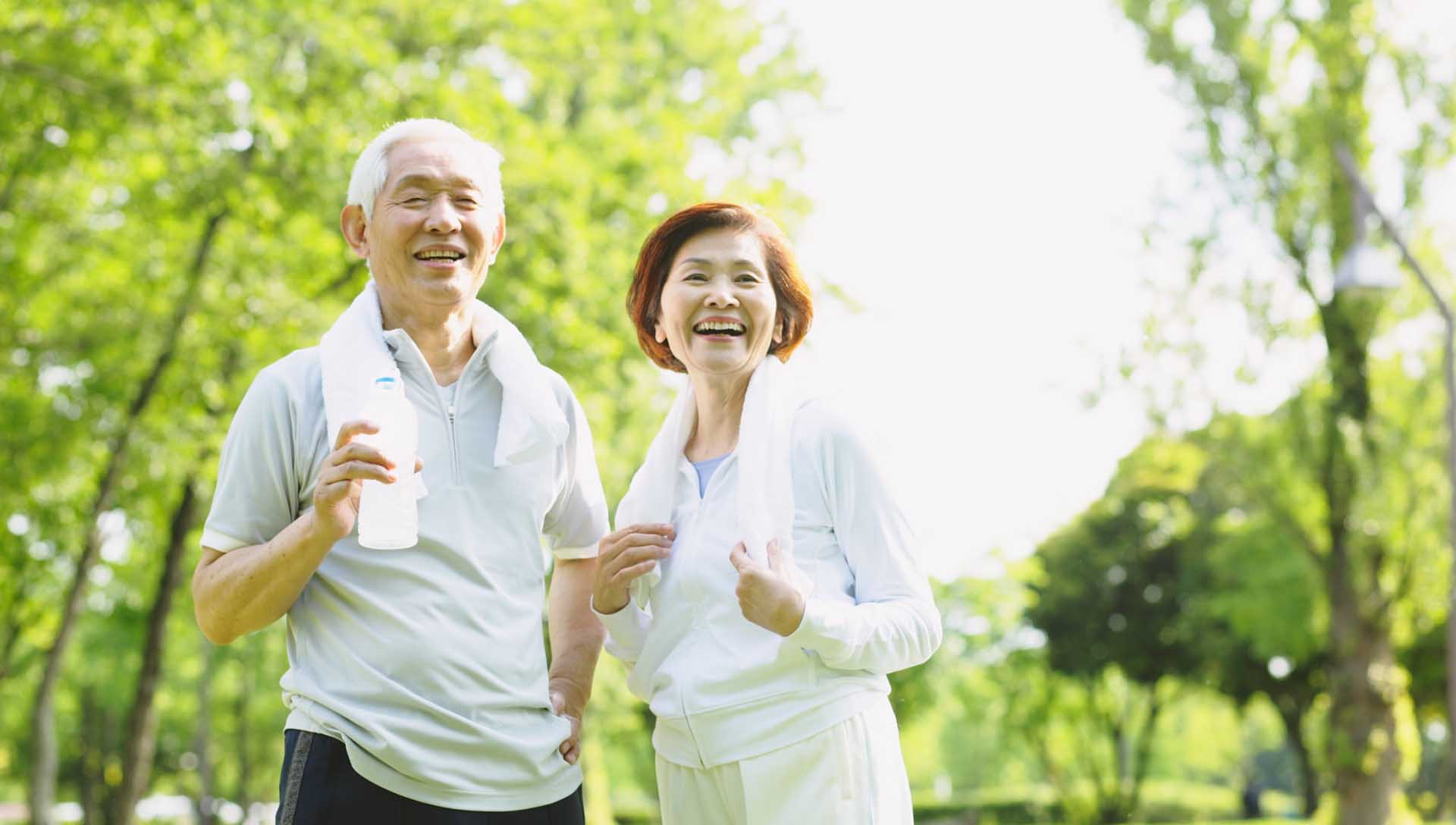 熟齡夫妻在綠意盎然的公園散步，呈現健康樂齡與整合照護的生活情境