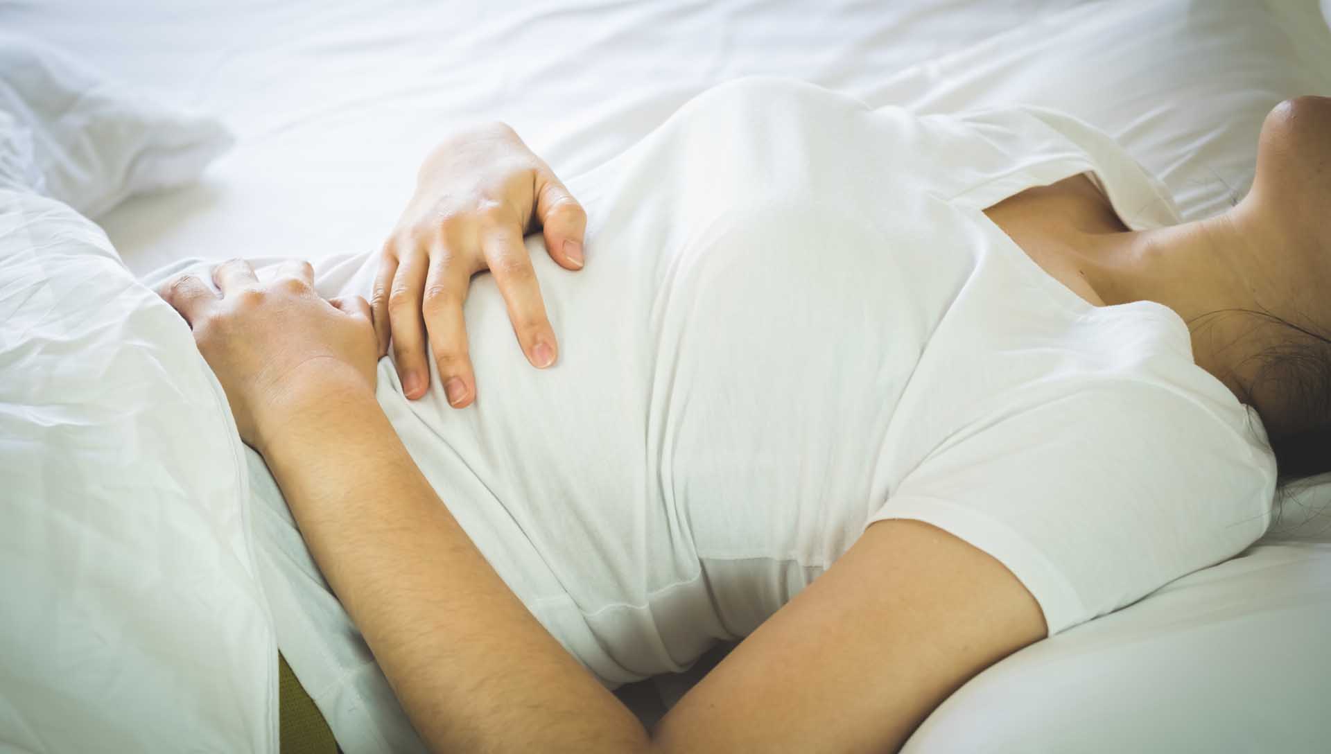 女性躺在床上雙手按住腹部，呈現胃痛與腸胃不適的情境